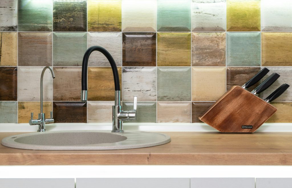 a kitchen sink with multi-coloured tiles behind it