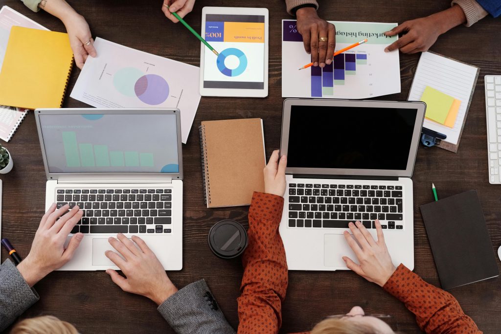 people with laptops gathered around a table full of papers with graphs