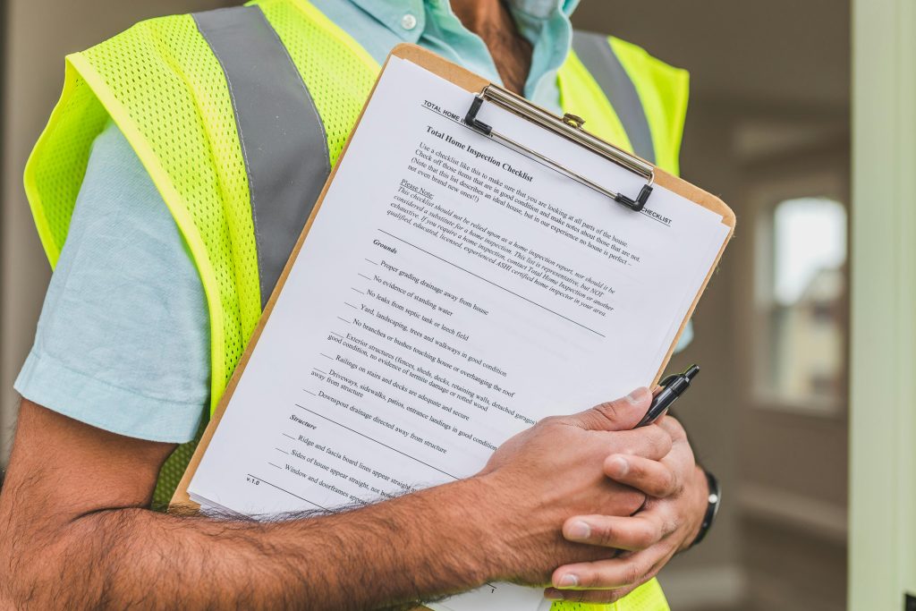 someone in a neon vest holding a clipboard with a home inspection checklist on it
