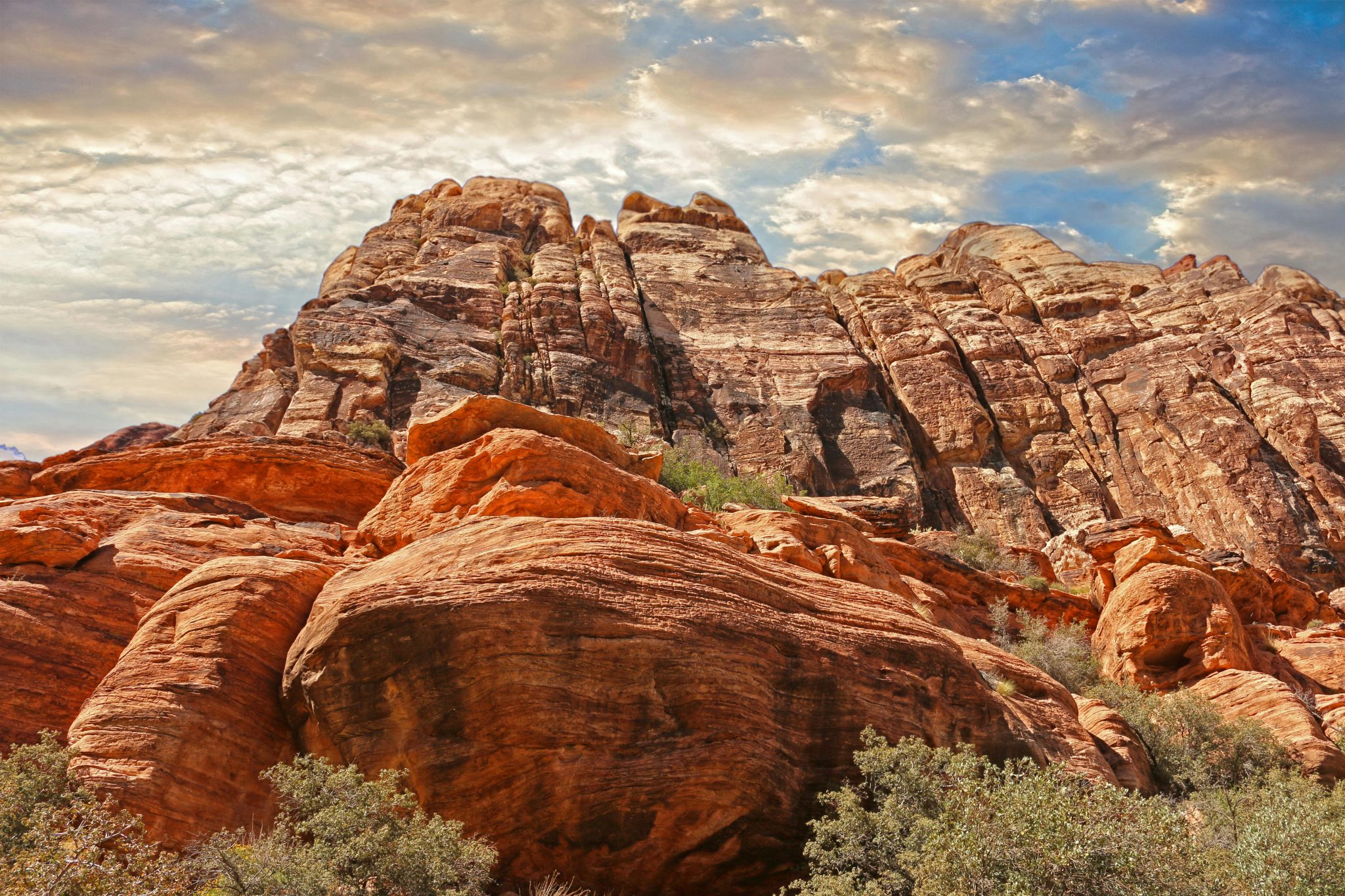 A large red rock formation with a cloudy blue sky in the background.